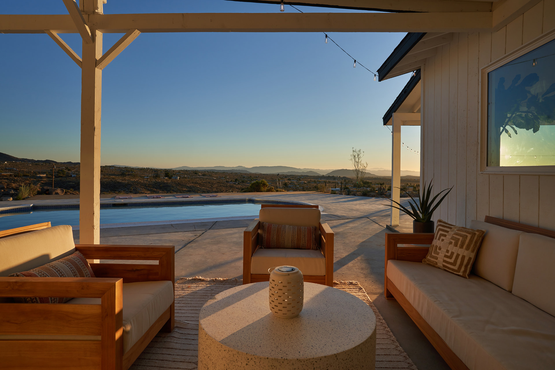Covered patio with wood sofas overlooking the pool and valley at dusk