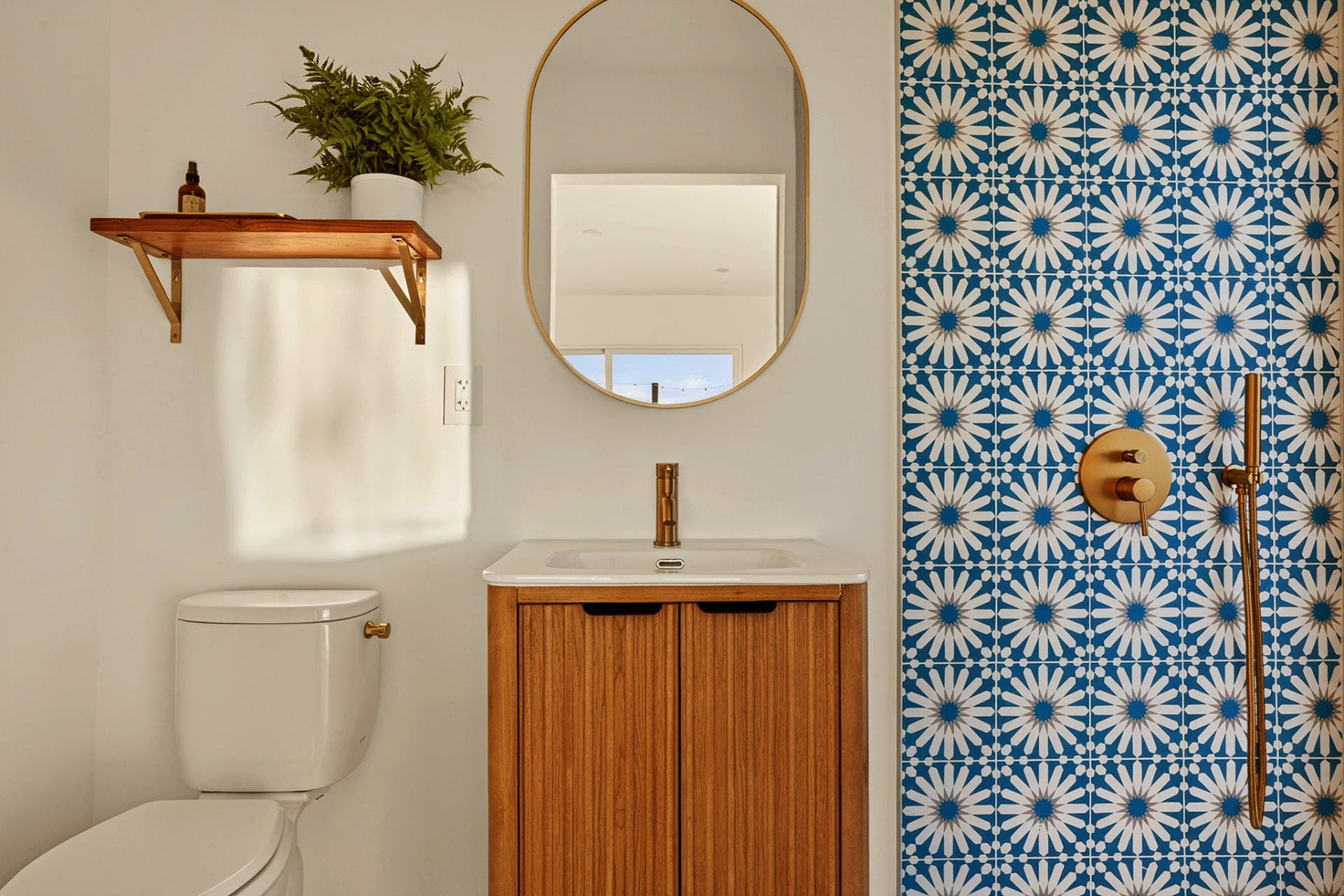 Bathroom vanity with brass faucet and blue patterned tile shower