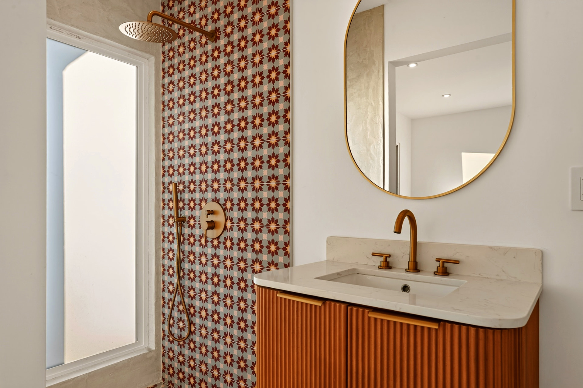 Bathroom with patterned cement tile shower, brass fixtures and vanity mirror