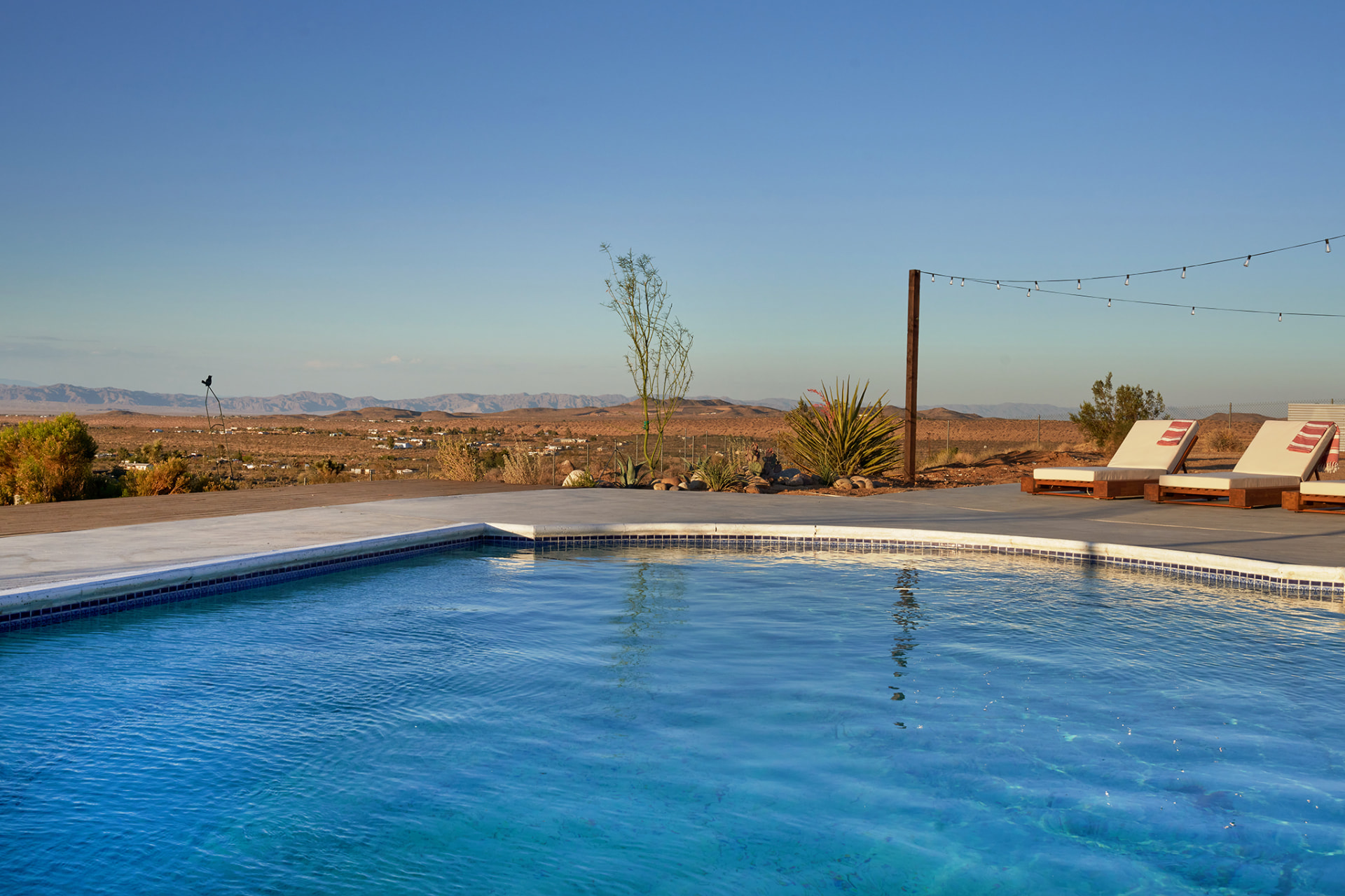 Pool with chaise loungers and string lights above desert views