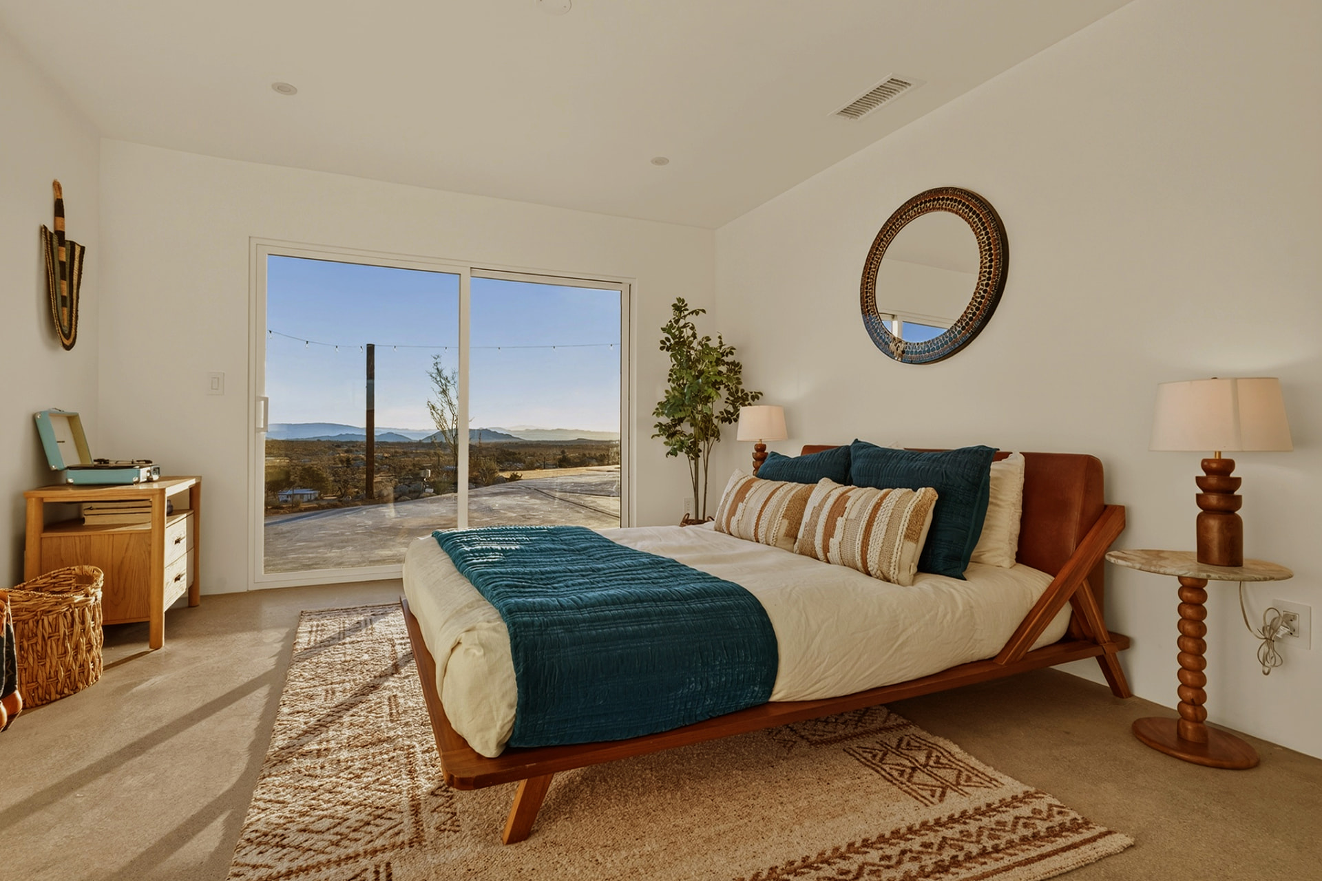 Bedroom with leather headboard, round mirror and sliding glass door to the valley view