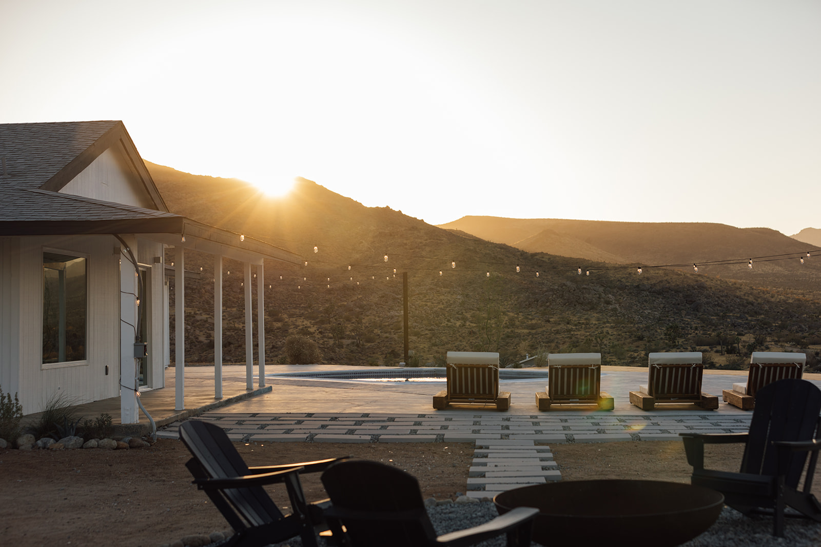 Sunburst over the ridge with string lights above the pool deck and firepit chairs